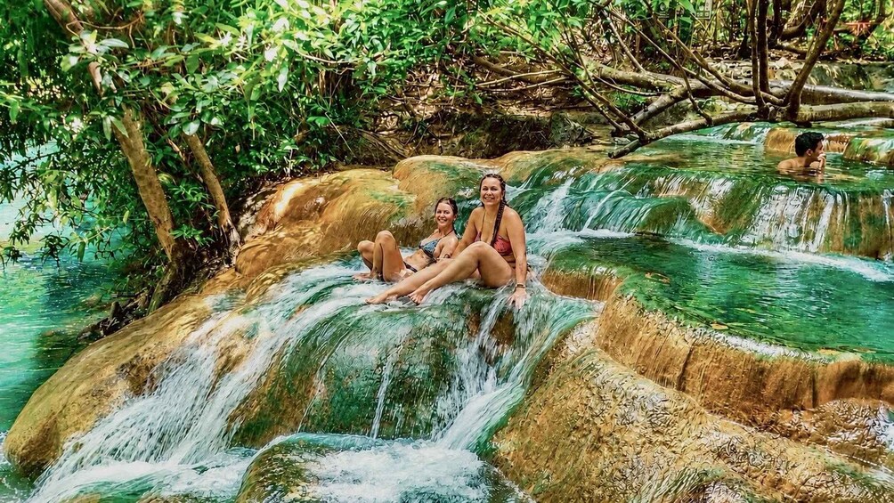 Two people sitting on a water cascade surrounded by greenery. 2