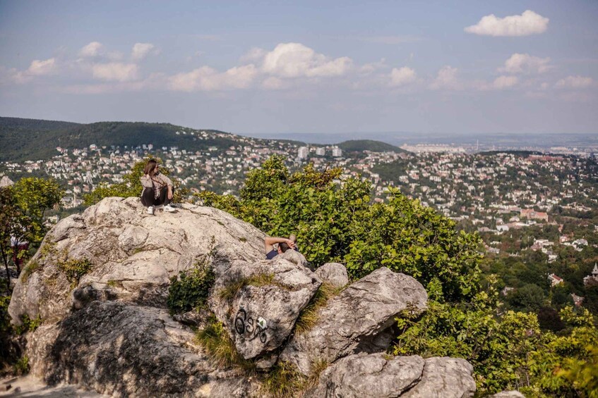 A person sitting on a rock with a cityscape in the background. 2