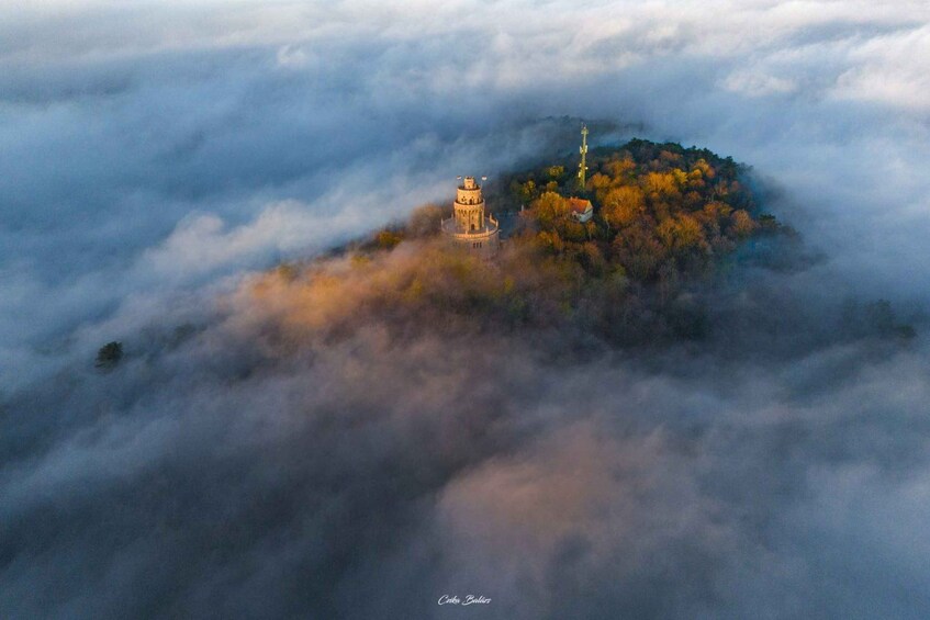 A tower on a hill surrounded by autumn foliage and clouds. 4