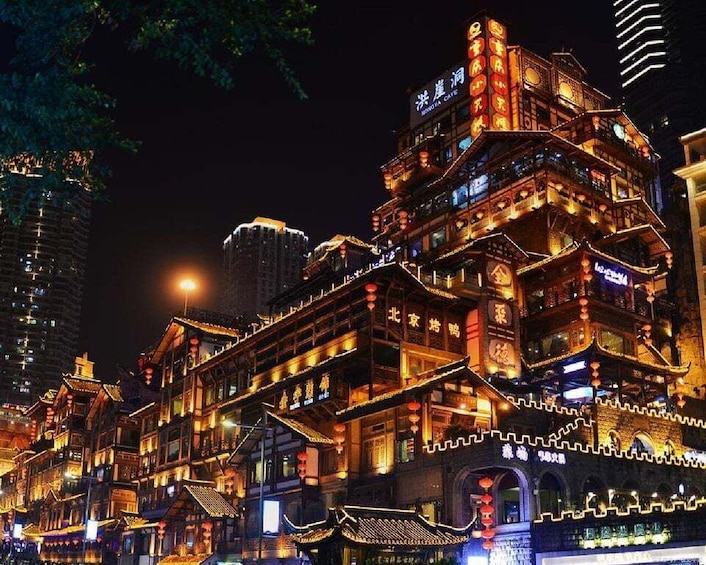 A brightly lit traditional building with multiple levels and ornate decorations, surrounded by modern high-rise buildings. 2