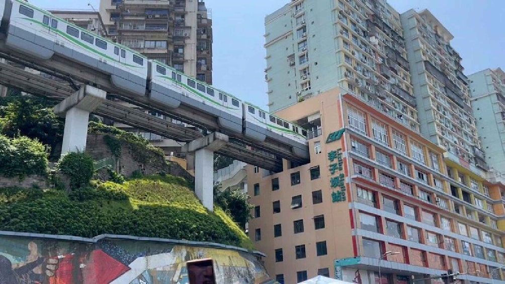 A train on an elevated track, a multi-story residential building, and a landscaped area with greenery. 5