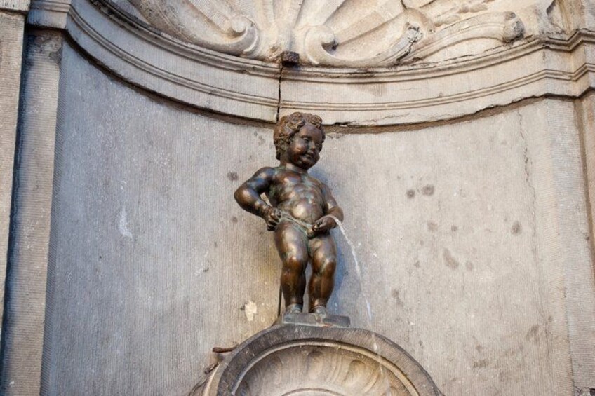 Een bronzen beeld van een kind met water dat uit zijn handen stroomt, geplaatst op een stenen constructie met versierde gravures. 4