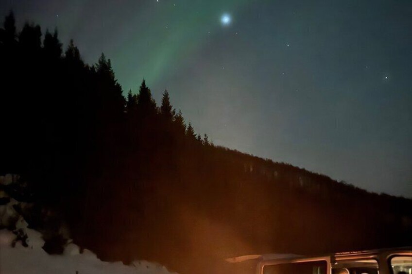 Una escena nocturna con la aurora boreal sobre una colina boscosa. 2