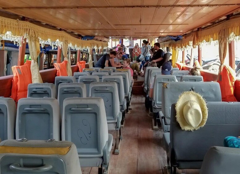 A ferry interior with rows of seats, some with hats on them, and passengers seated and standing. 3