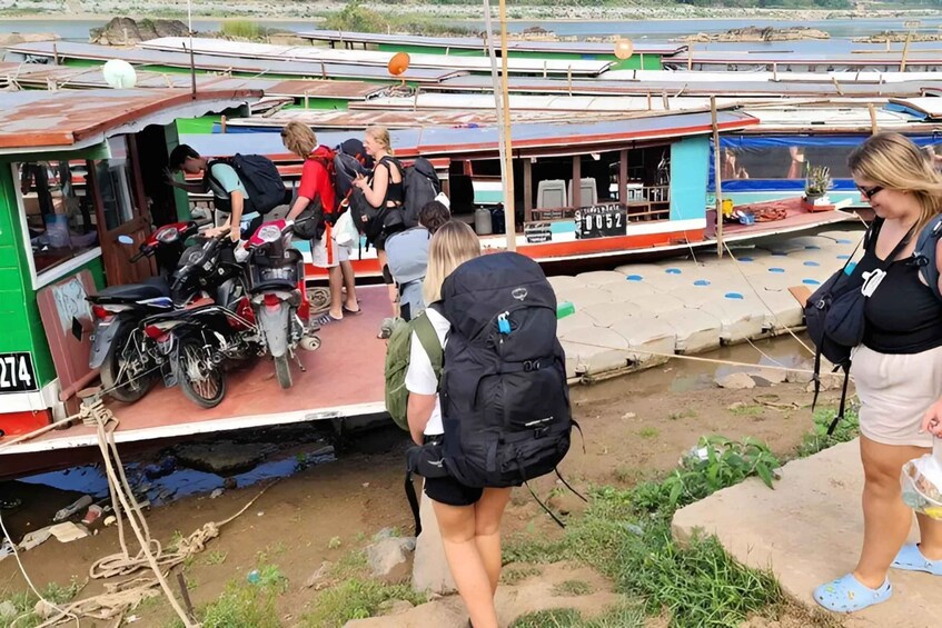 A group of people boarding a boat with a motorcycle and a green and red structure. 1