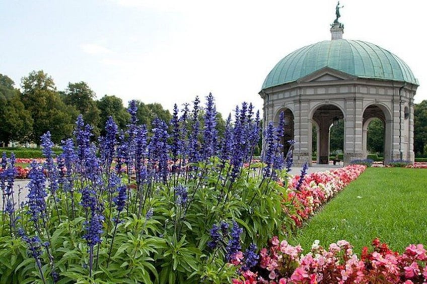 Ein Pavillon mit einer grünen Kuppel, umgeben von üppigen Blumen und einem gepflegten Rasen. 4