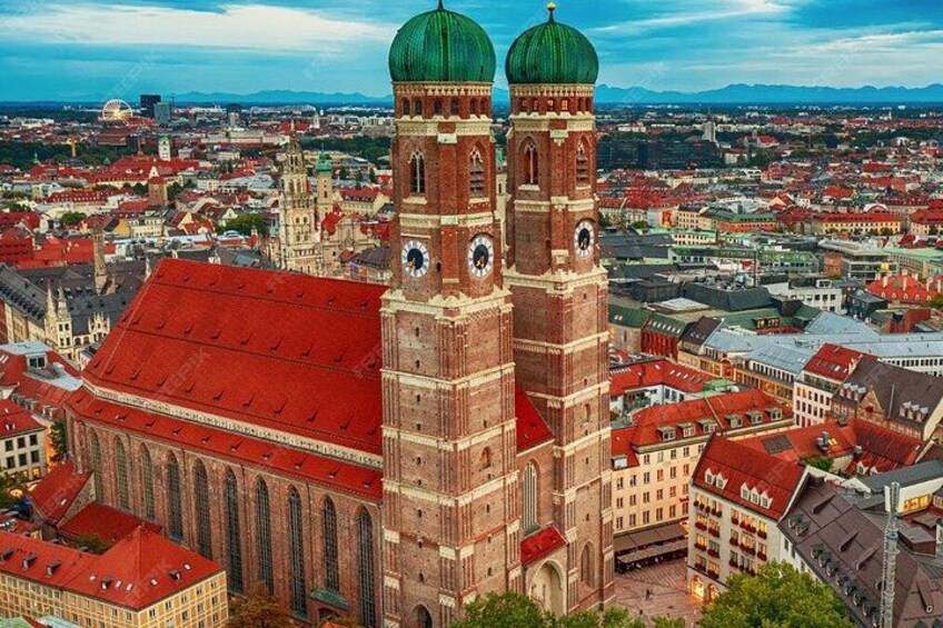 Ein großes Gebäude mit rotem Dach und zwei grünen Türmen, umgeben von einer Stadtlandschaft. 5
