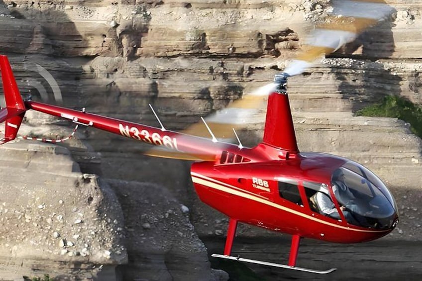 En rød helikopter med ski lander på et klippefyldt terræn. 2