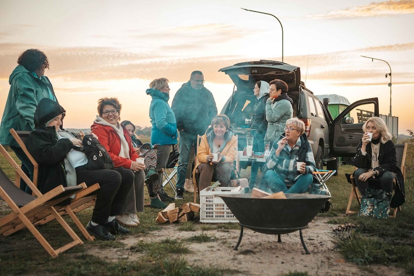 A group of people gathered around a campfire in an outdoor setting with a vehicle in the background. 5