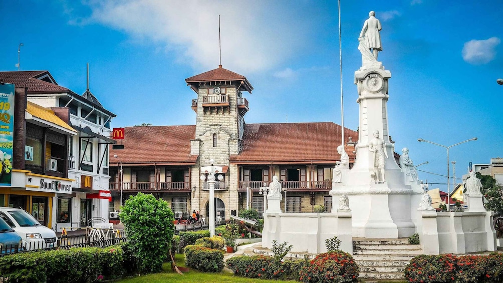 A town square with a clock tower, a statue, and surrounding buildings. 1