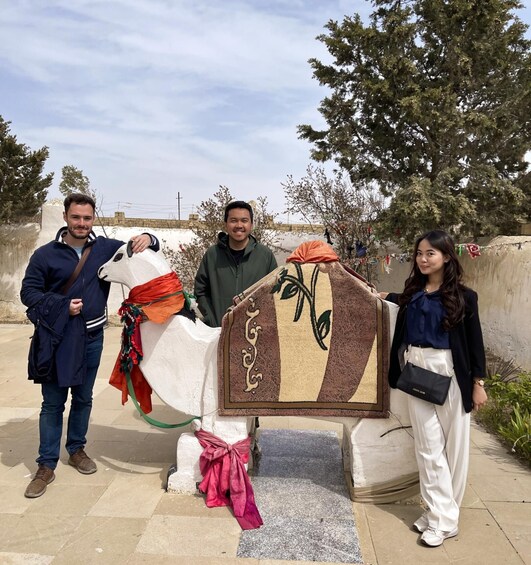Three people standing next to a decorated horse statue. 1