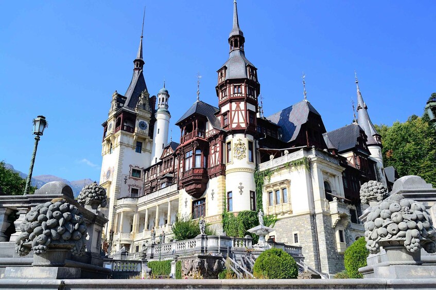 A historic building with multiple spires and a balcony, surrounded by statues and greenery. 3