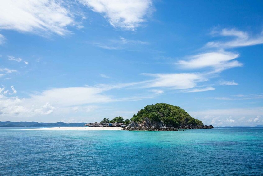 A tropical island with clear turquoise waters, a small beach, and lush greenery. 1