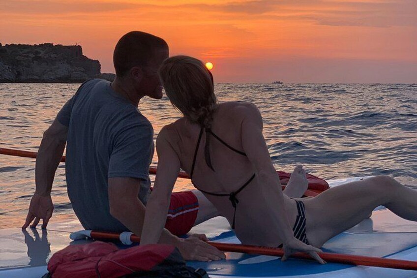 A couple sitting on a boat at sunset with the ocean and a rocky coastline in the background. 3