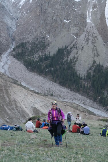A hiker in a purple jacket with a backpack, surrounded by other hikers in a mountainous area with sparse vegetation and rocky terrain. 2