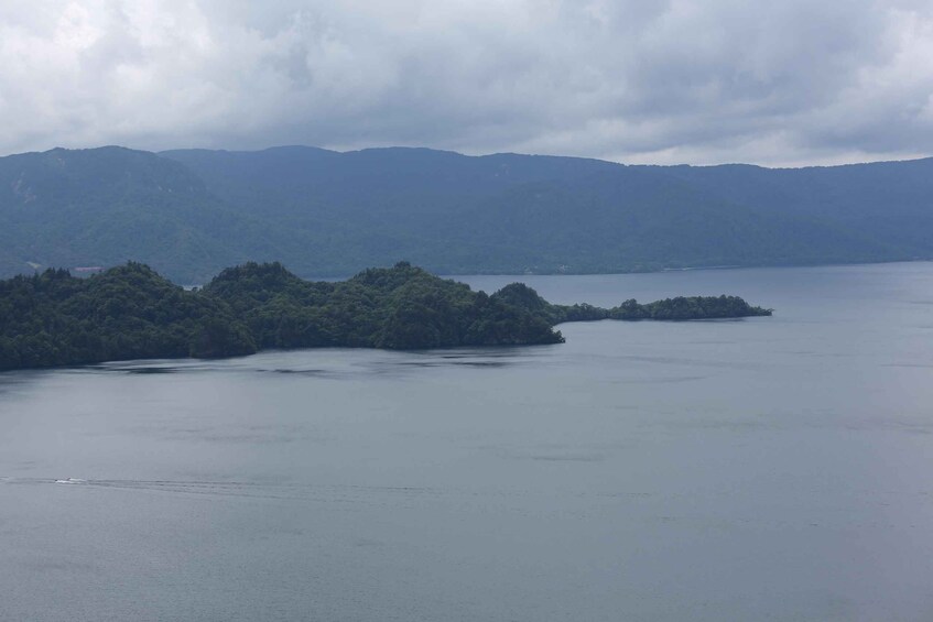A calm lake surrounded by forested hills and a cloudy sky. 1