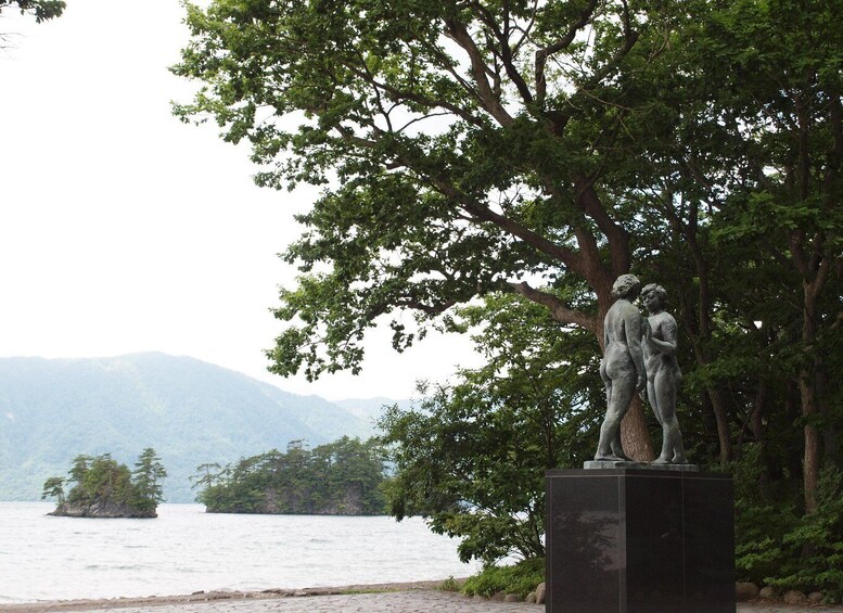 A statue of two figures by a lake with mountains in the background. 5