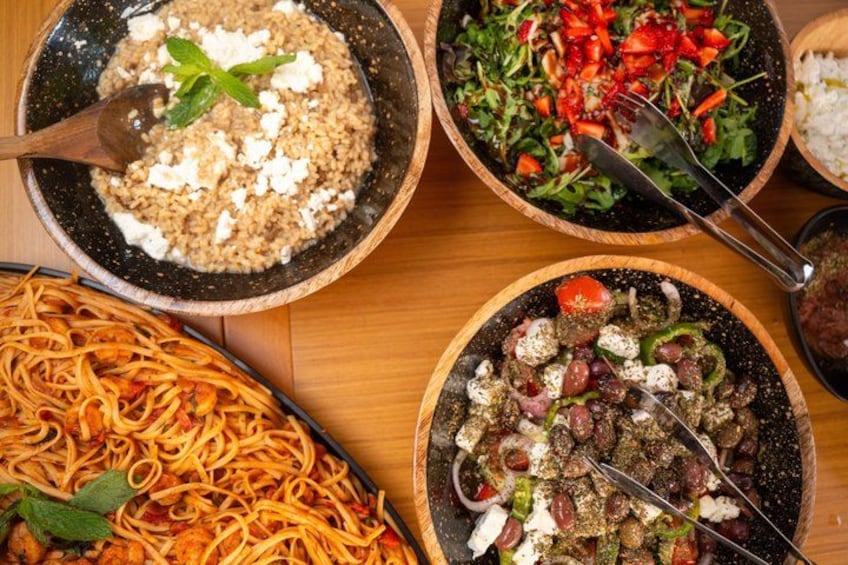 A variety of dishes including a bowl of rice with feta cheese, a salad with tomatoes and greens, a plate of spaghetti, and a dish with olives and vegetables. 5
