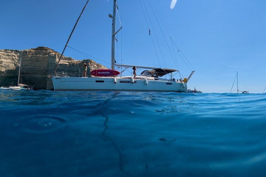 A white sailboat with a red lifebuoy on calm blue waters near a rocky coastline. 3