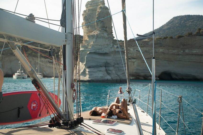 A sailboat with a person lying on the deck, rocky cliffs in the background, and calm blue water. 2