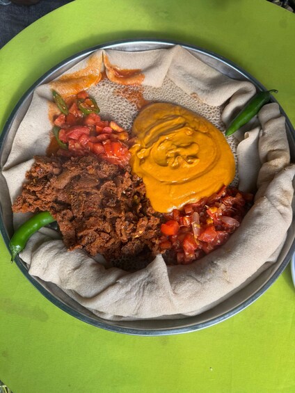 A traditional Ethiopian meal on a plate with injera, a yellow lentil stew, a red tomato-based dish, and a dark meat dish. 2