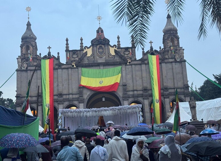 A historic church with a large flag and people under umbrellas. 1