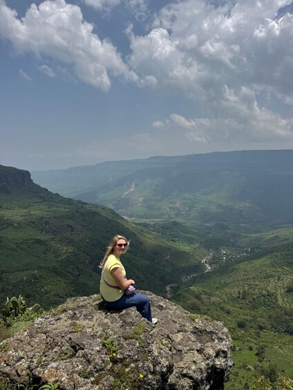 A person sitting on a rocky outcrop overlooking a valley with green hills and a river. 5