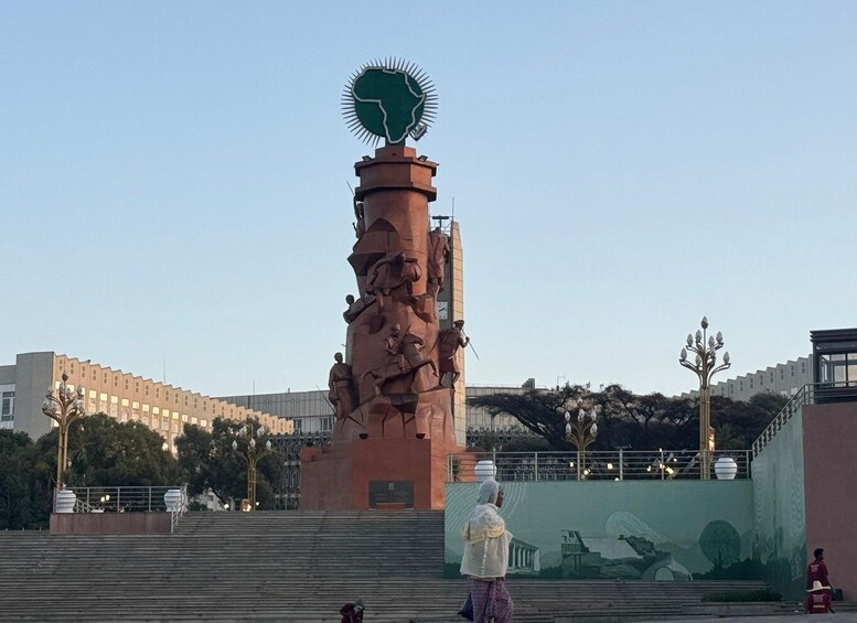 A large statue with a green top, surrounded by steps and a mural. 5
