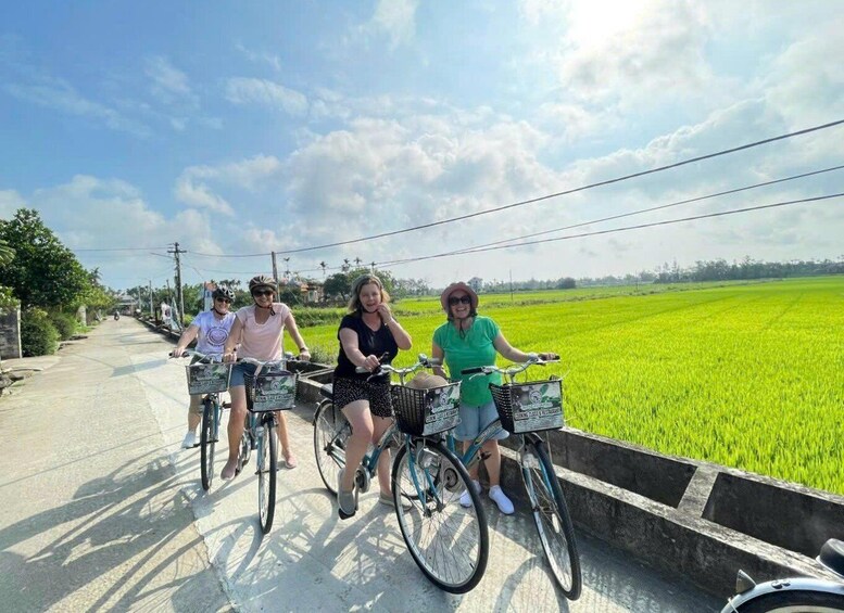 Four people riding bicycles on a road with a green field on one side. 5