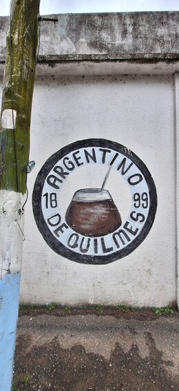 A wall with a circular emblem featuring a pot and the text 'ARGENTINO 18 99 DE OUILLES.' 3