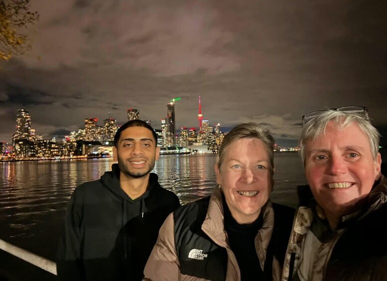 Three people standing by a waterfront with a city skyline in the background. 1