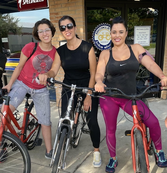 Three people with bicycles in front of a bike shop. 1