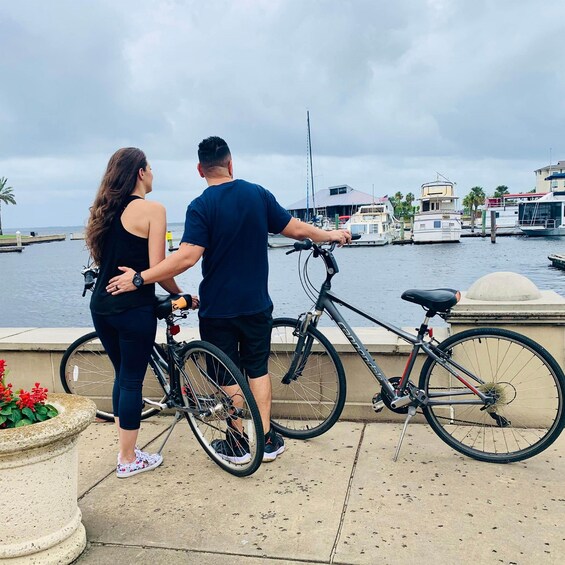 Two people standing by a waterfront with bicycles, overlooking a marina with boats and buildings. 4