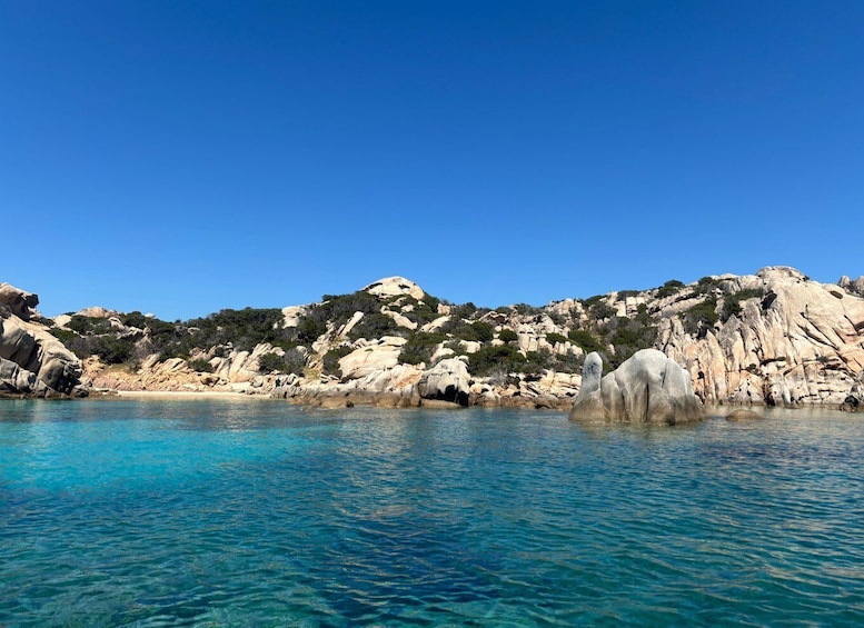 A coastal landscape with clear turquoise waters, rocky formations, and a clear blue sky. 4