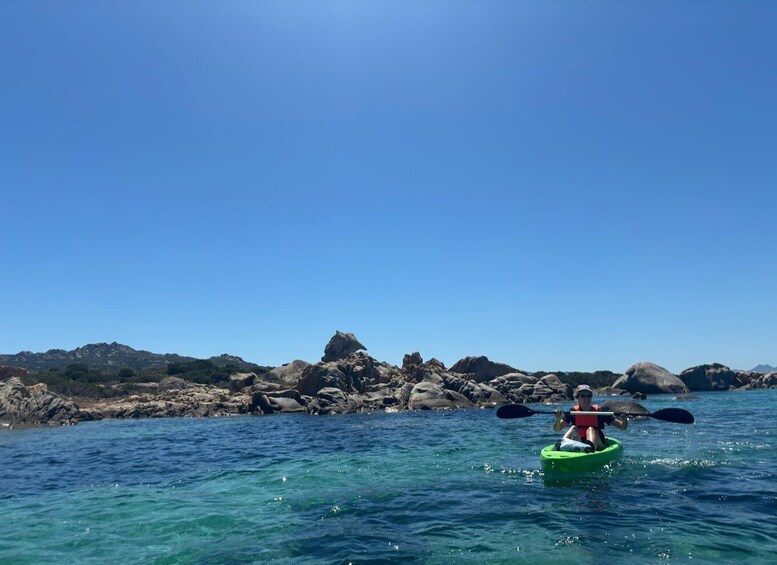A person kayaking on clear blue water with rocky outcrops in the background. 1