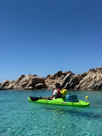A person kayaking in clear water with a rocky shoreline in the background. 2
