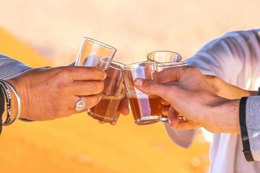Two hands holding glasses of amber liquid, likely a beverage, against a blurred background. 3