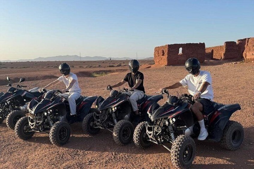 Three people on quad bikes in a desert with ancient ruins in the background. 4
