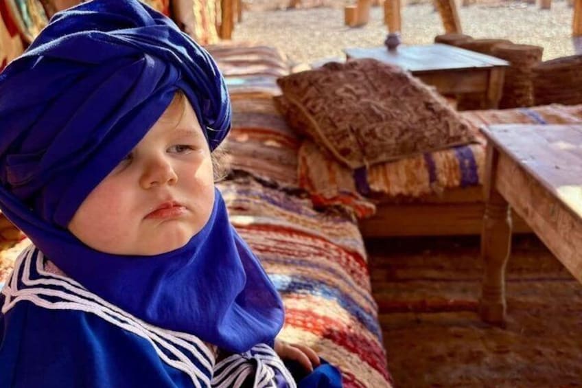 A child in traditional attire sitting on a patterned rug. 2