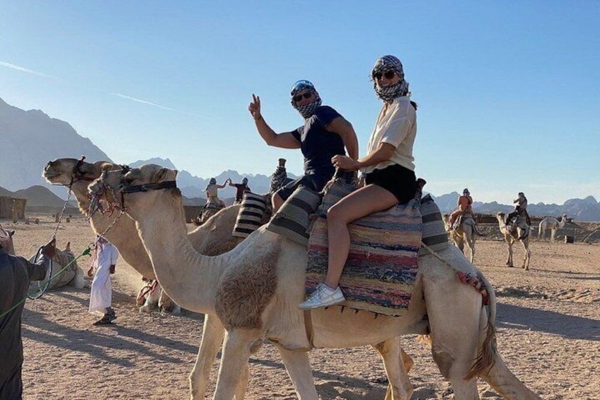 Due persone cavalcano dromedari in un deserto con montagne sullo sfondo. 3