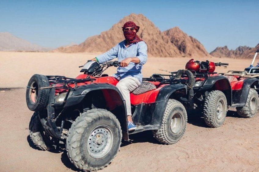 Una persona guida un ATV nel deserto, con montagne sullo sfondo. 1