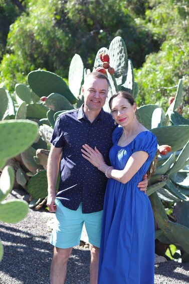 A couple standing in front of large cacti with green leaves and red fruits. 5