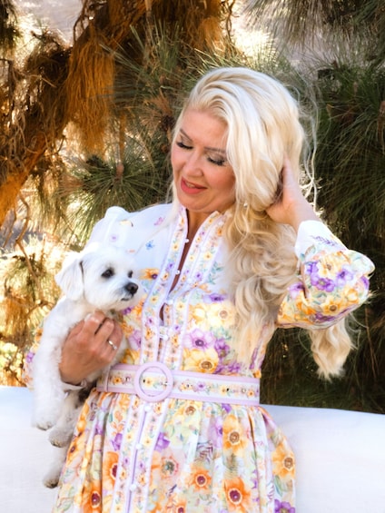 A person in a floral dress holding a small white dog. 1