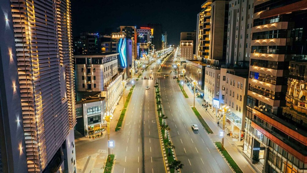 A nighttime cityscape with illuminated buildings and a wide, empty street. 3