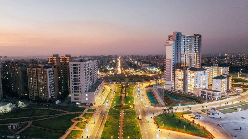 A cityscape at dusk with illuminated buildings, a central roundabout, and surrounding greenery. 2