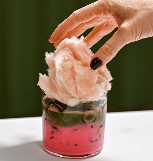 A hand holding cotton candy over a glass with a pink drink. 4