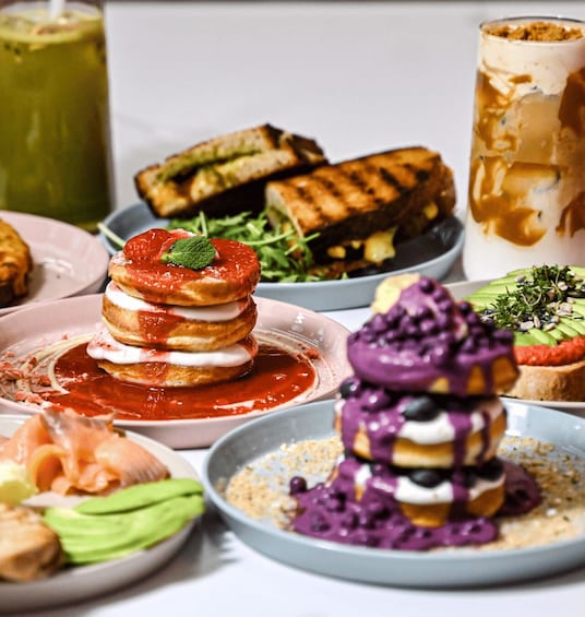 A variety of desserts and dishes, including a stack of pancakes with strawberries, a bowl of purple dessert, and a glass of iced coffee. 1
