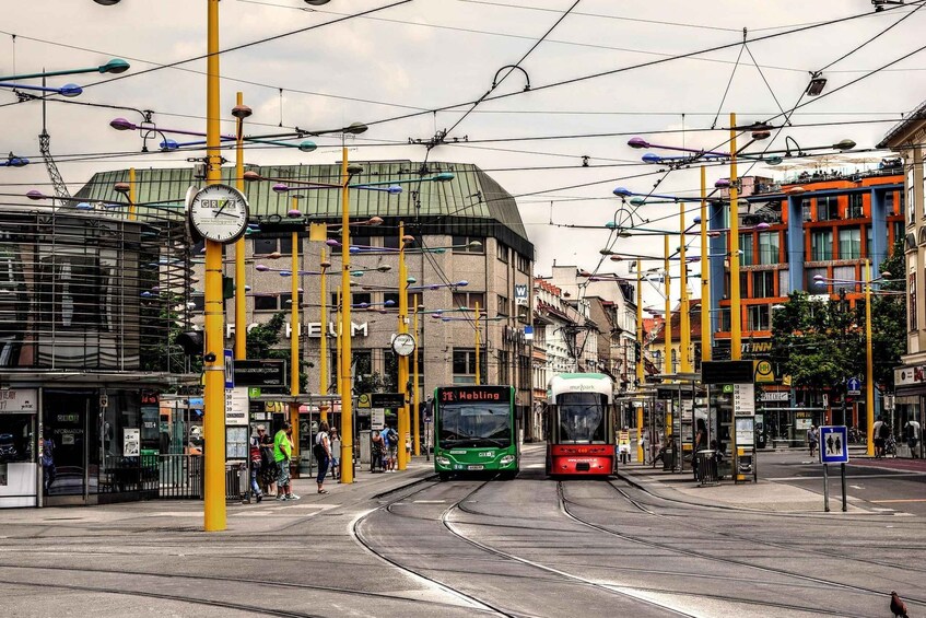 A tram station with trams, a clock, and urban buildings. 4