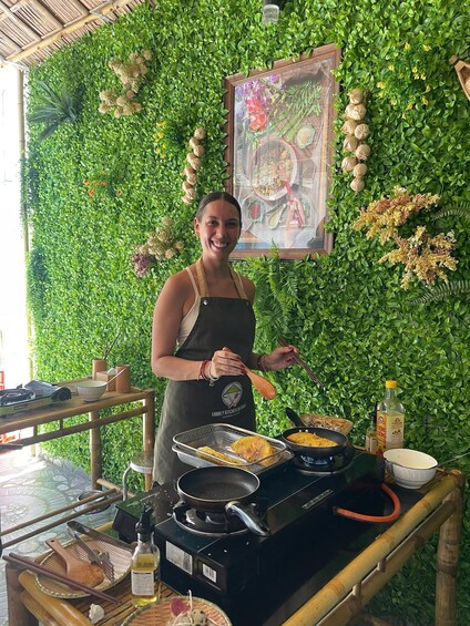 A person cooking in a kitchen with a green leafy wall backdrop and a painting above the stove. 2