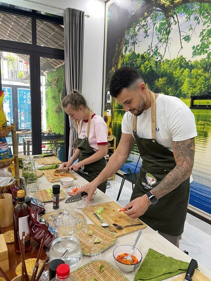 Two people preparing food at a table with various ingredients and kitchen tools. 3